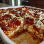 Close-up of baked pepperoni pizza dip in a white dish with cheese pull and melted mozzarella.