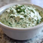 Close-up of creamy, fresh dill dip generously garnished with chopped dill in a white serving bowl.