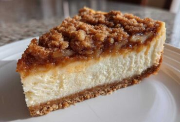 A perfect slice of amazing apple pie cheesecake featuring a creamy white layer, graham cracker crust, and a thick cinnamon apple crumble topping.
