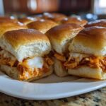 Close-up of gooey, melted cheese oozing over shredded chicken filling in fresh rolls for buffalo chicken sliders.