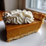 A perfect slice of rich, orange-hued butterscotch pie topped with a swirl of whipped cream.