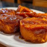 Four portions of rich, orange candied yams covered in a thick, glossy brown sugar glaze, served on a white plate.