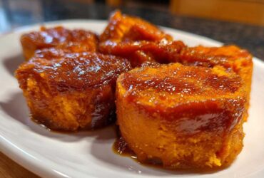Four portions of rich, orange candied yams covered in a thick, glossy brown sugar glaze, served on a white plate.