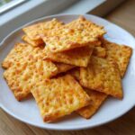 A stack of golden, crispy homemade cheese crackers piled high on a white plate.