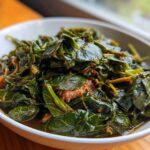 A close-up of tender, dark green collard greens simmered in a rich broth, served in a white bowl.