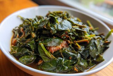 A close-up of tender, dark green collard greens simmered in a rich broth, served in a white bowl.