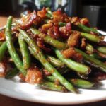 A close-up of glossy, vibrant green beans tossed with crispy, caramelized bacon pieces.