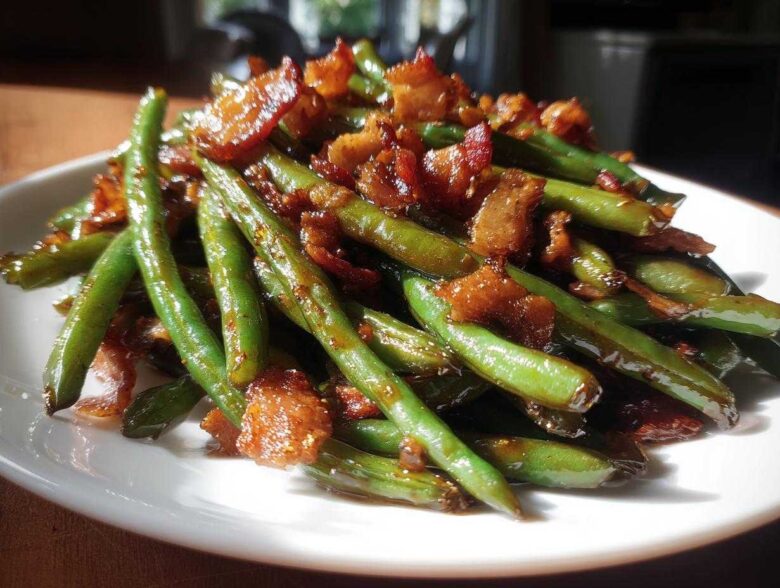 A close-up of glossy, vibrant green beans tossed with crispy, caramelized bacon pieces.