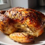 A whole roasted chicken with deeply browned, herbed skin resting on a white plate, ready to serve.
