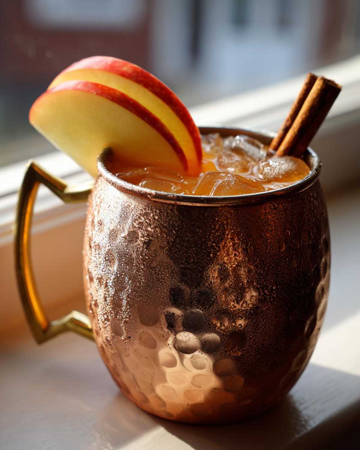 A frosty copper mug filled with an apple cider Moscow mule, garnished with apple slices and cinnamon sticks.