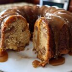 A rich apple dapple cake, shaped like a bundt, with a slice cut out, generously covered in dripping caramel sauce.
