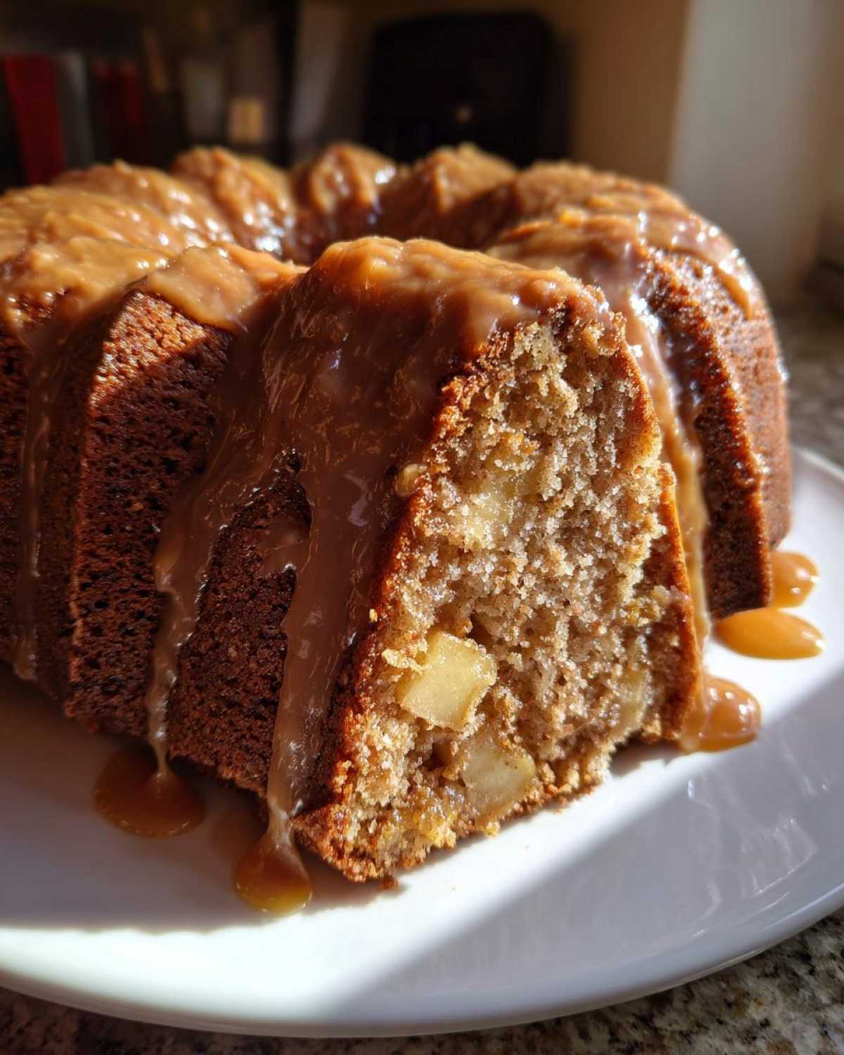 A close-up of a slice cut from a bundt-style apple dapple cake, topped with thick caramel sauce.