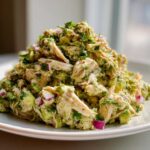 Close-up of a generous serving of creamy avocado chicken salad mixed with chunks of avocado, red onion, and cilantro.