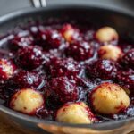 Close-up of golden Blackberry Dumplings simmering in a rich, dark purple blackberry sauce in a pan.