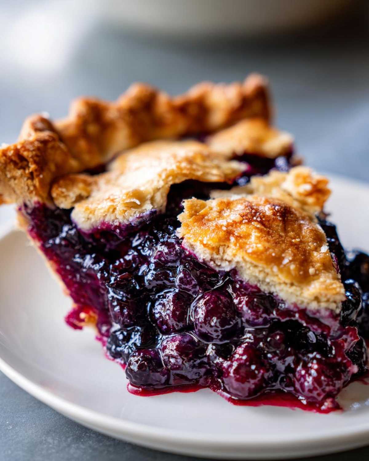 Close-up of a juicy slice of blueberry pie recipe, showing rich purple filling and golden crust.