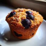 Close-up of a single, golden-brown blueberry protein muffin topped with coarse sugar.