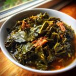 Close-up of a white bowl filled with rich, dark green collard greens cooked in savory broth with pieces of smoked meat.