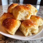 A stack of fluffy, golden-brown buttery rolls glistening with a sweet glaze on a white plate.