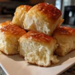 A stack of fluffy, golden-brown buttery rolls brushed with a shiny glaze, showing their soft interior.
