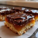 Close-up of a layered caramel ritz cracker christmas cookies bar with a buttery base, thick caramel, and chocolate topping.