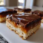 A close-up of a square of caramel ritz cracker christmas cookies showing the shortbread base, thick caramel layer, and chocolate topping.