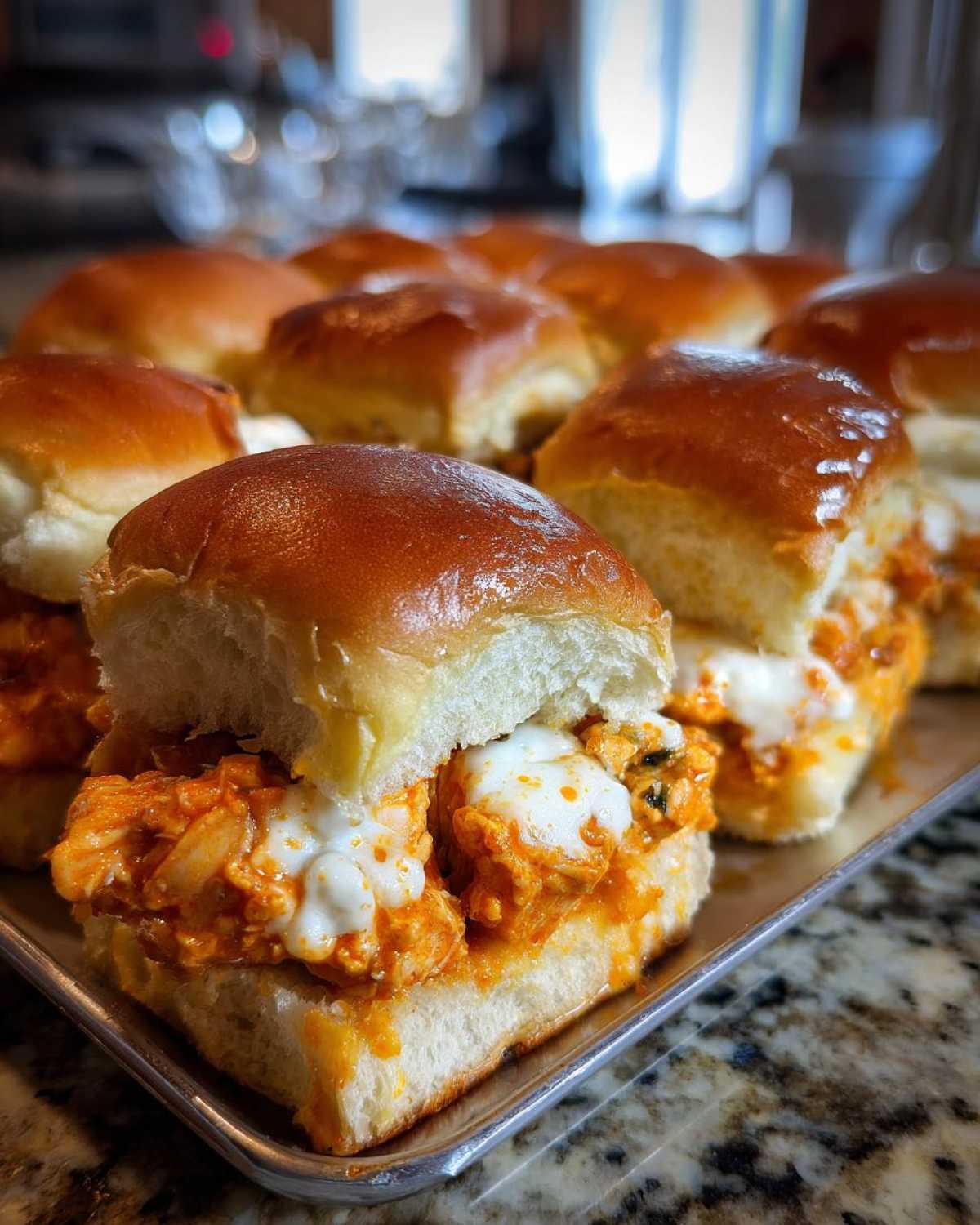 A close-up view of freshly baked buffalo chicken sliders filled with orange sauce and melted white cheese on sweet rolls.
