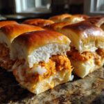 Close-up of freshly baked buffalo chicken sliders filled with orange sauce and melted white cheese on a marble surface.