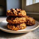 A stack of three chewy banana oatmeal cookies topped with melted chocolate chips resting on a small plate.