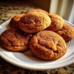 A stack of freshly baked, chewy snickerdoodle cookies generously coated in cinnamon sugar, resting on a white plate.