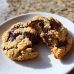 Close-up of a chewy vegan chocolate chip cookie broken in half, revealing melted chocolate pools.