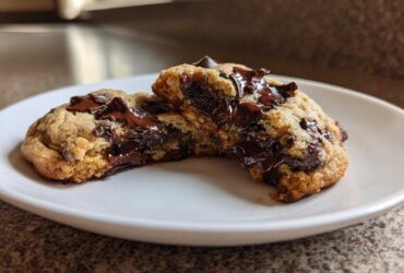 A chewy vegan chocolate chip cookie broken in half showing a gooey, melted chocolate center.