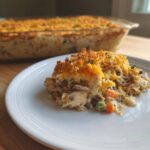 A serving of creamy chicken wild rice casserole topped with golden breadcrumbs and cheese on a white plate.