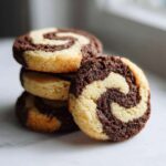 A stack of three chocolate and vanilla swirl pinwheel cookies, with one cookie leaning against the stack.