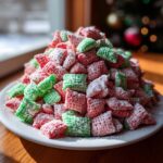 A mound of red and green Christmas puppy chow coated in powdered sugar, set against a bright window.