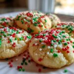 A close-up photo of several soft, round christmas sprinkle sugar cookies topped with red, white, and green holiday sprinkles.