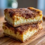 Two stacked squares of creamy churro cheesecake topped generously with cinnamon sugar.