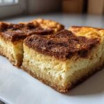 Close-up of two rich, thick slices of churro cheesecake on a white plate, showing the crust, creamy filling, and cinnamon sugar topping.