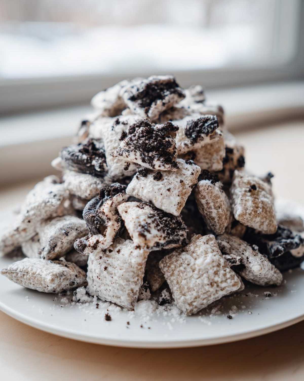 A close-up of a tall pile of cookies and cream puppy chow coated in powdered sugar and dark cookie crumbs.