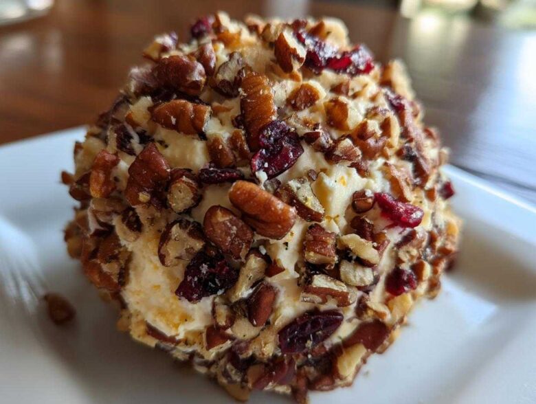 A close-up view of a perfectly formed cranberry pecan cheese ball coated in chopped pecans and dried cranberries.