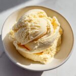 Close-up overhead shot of creamy, pale yellow banana ice cream scooped into a light ceramic bowl.