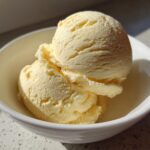 Close-up of two scoops of creamy, pale yellow banana ice cream in a small white bowl.