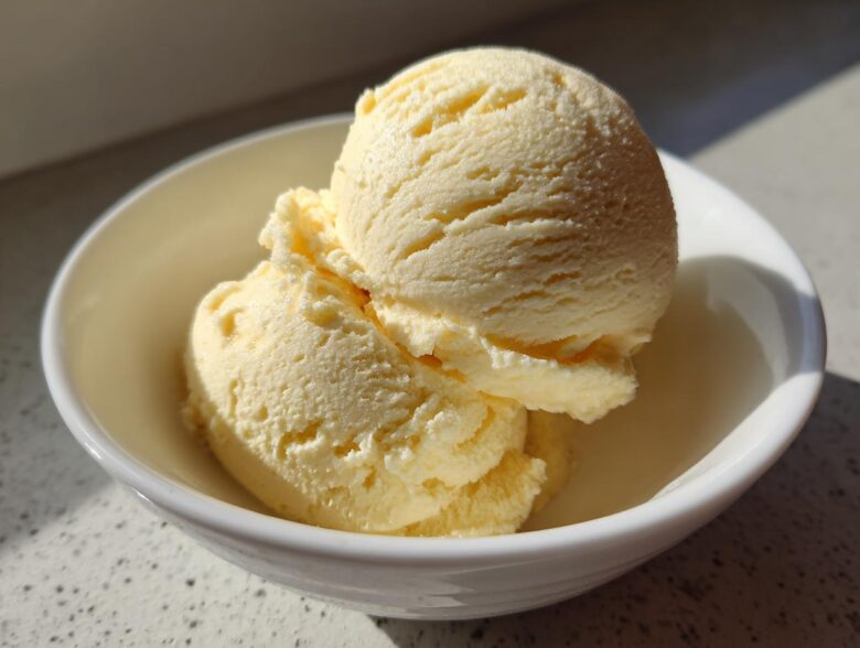 Close-up of two scoops of creamy, pale yellow banana ice cream in a small white bowl.