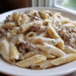 A close-up shot of a white bowl filled with creamy beef pasta made with penne, topped with ground meat and parsley.