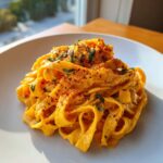A close-up of creamy butternut squash pasta tossed with fresh herbs and sprinkled with paprika on a white plate.