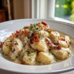 A close-up of creamy crack chicken gnocchi generously topped with crispy bacon bits and fresh parsley.
