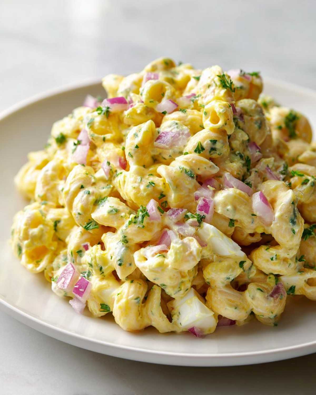 A close-up of a creamy deviled egg pasta salad featuring elbow macaroni, chopped red onion, and parsley.