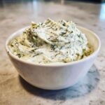 Close-up of a white bowl filled with creamy dill dip generously mixed with fresh green dill herbs.
