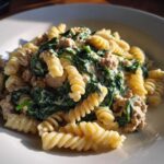 Close-up of creamy ground turkey pasta mixed with wilted spinach, served in a white bowl.
