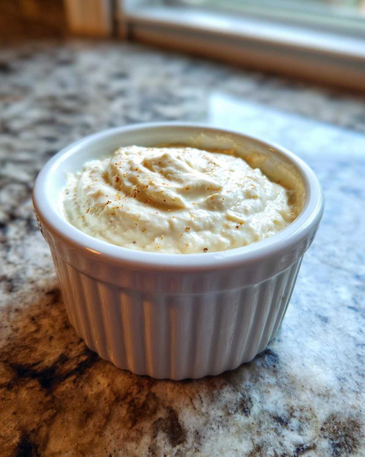 A small white ramekin filled with creamy horseradish sauce for prime rib, sprinkled with spices.