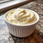 A close-up of creamy, white horseradish sauce for prime rib, garnished with dark specks, served in a small white fluted ramekin.